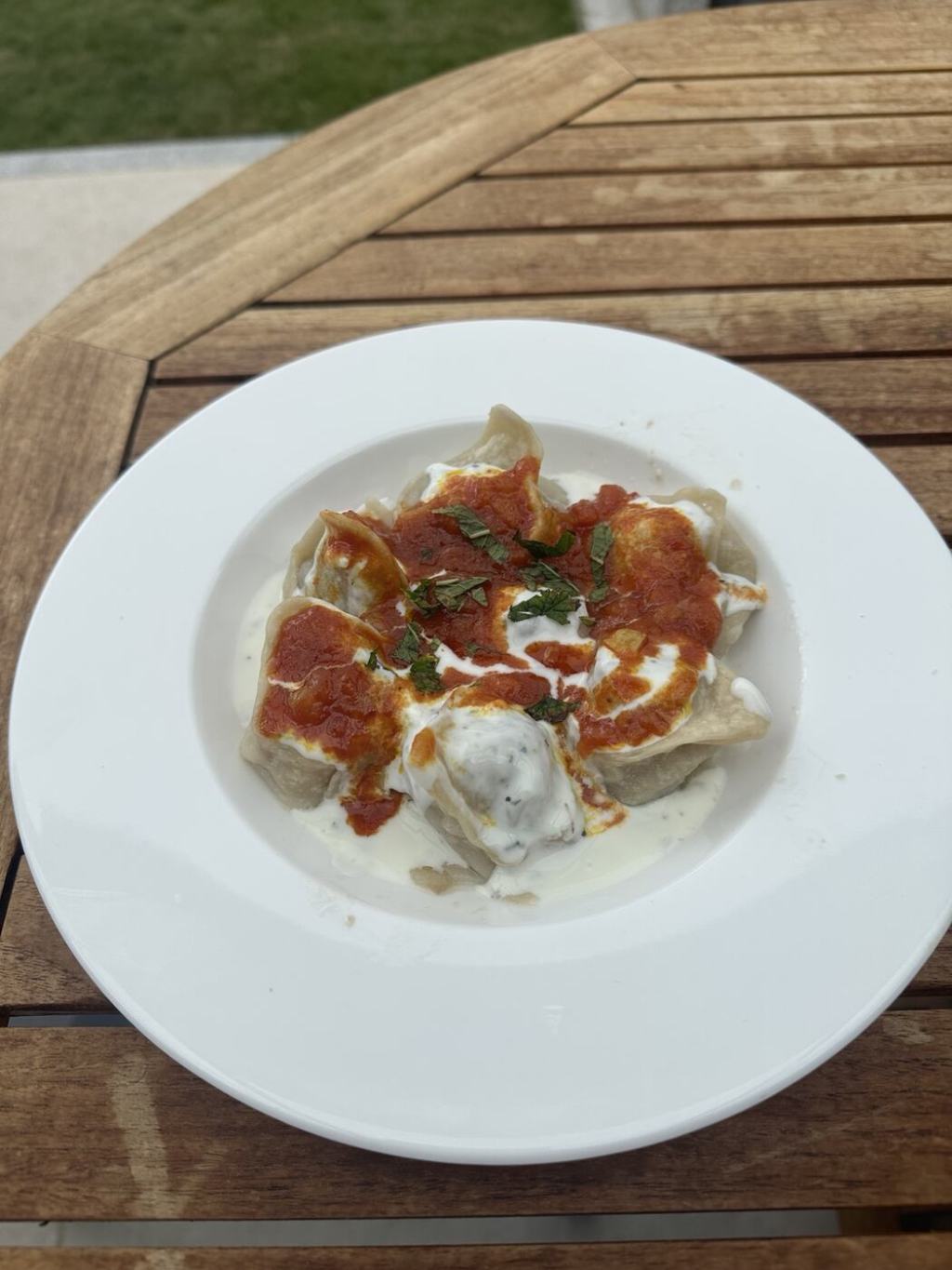 Homemade Afghan Mantu topped with yoghurt sauce, tomato sauce and mint.