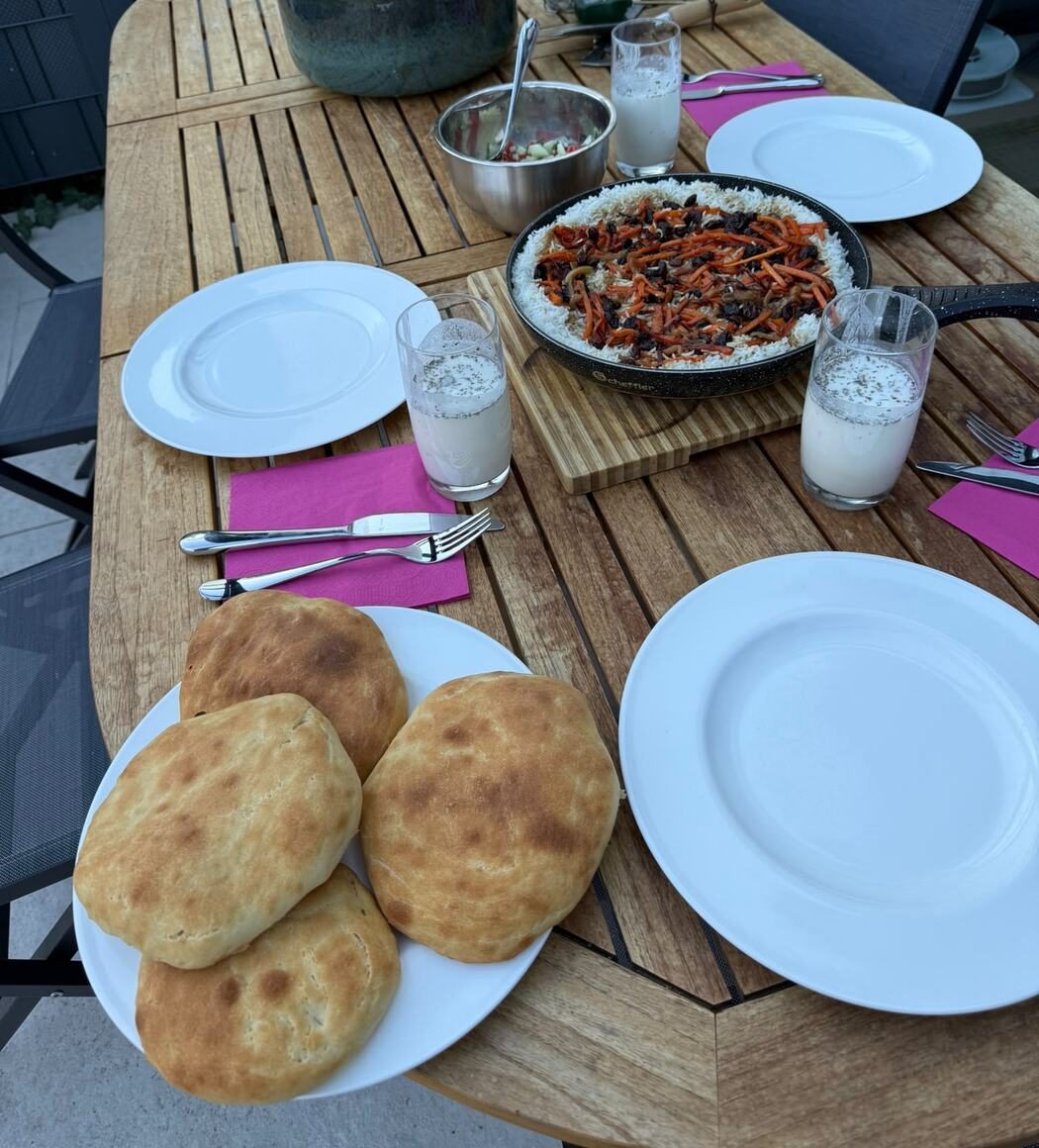 A family table set with homemade Afghan dishes, including Kabuli Palaw, naan, salad and doogh.