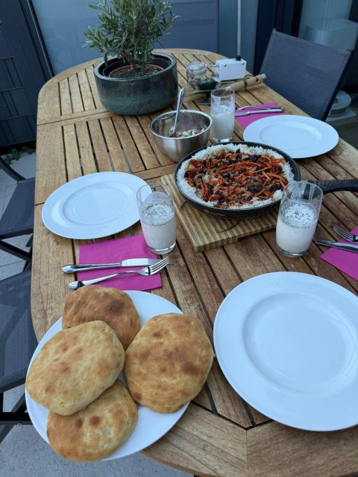 A family table set with homemade Afghan dishes, including Kabuli Palaw, naan, salad and doogh.
