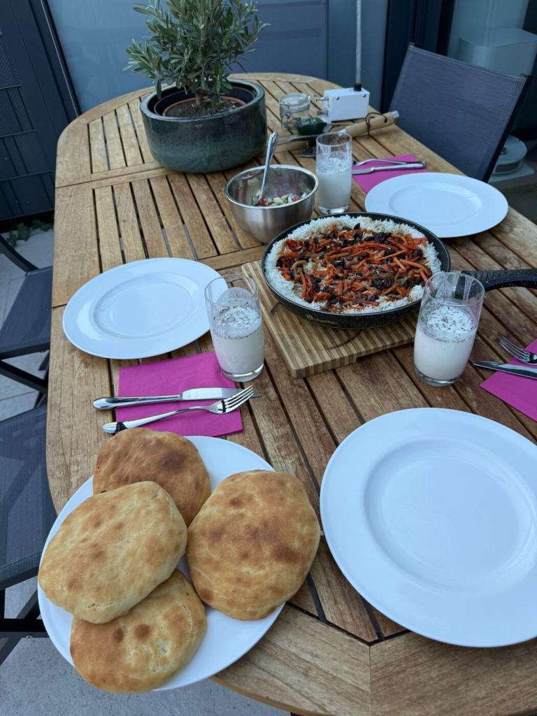 A family table set with homemade Afghan dishes, including Kabuli Palaw, naan, salad and doogh.
